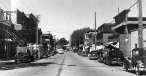 Plusieurs voitures stationnées sur la Rue Principale en 1946. À l'époque, on devait apposer la plaque d'immatriculation à l'avant et à l'arrière de celles-ci - Fonds studio RC. La Société d'histoire de Magog
